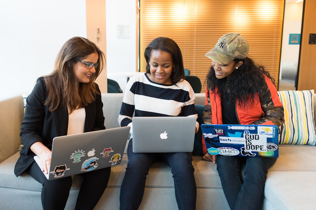 three-women-sitting-on-sofa-with-macbook-fpqlxqtjkqu